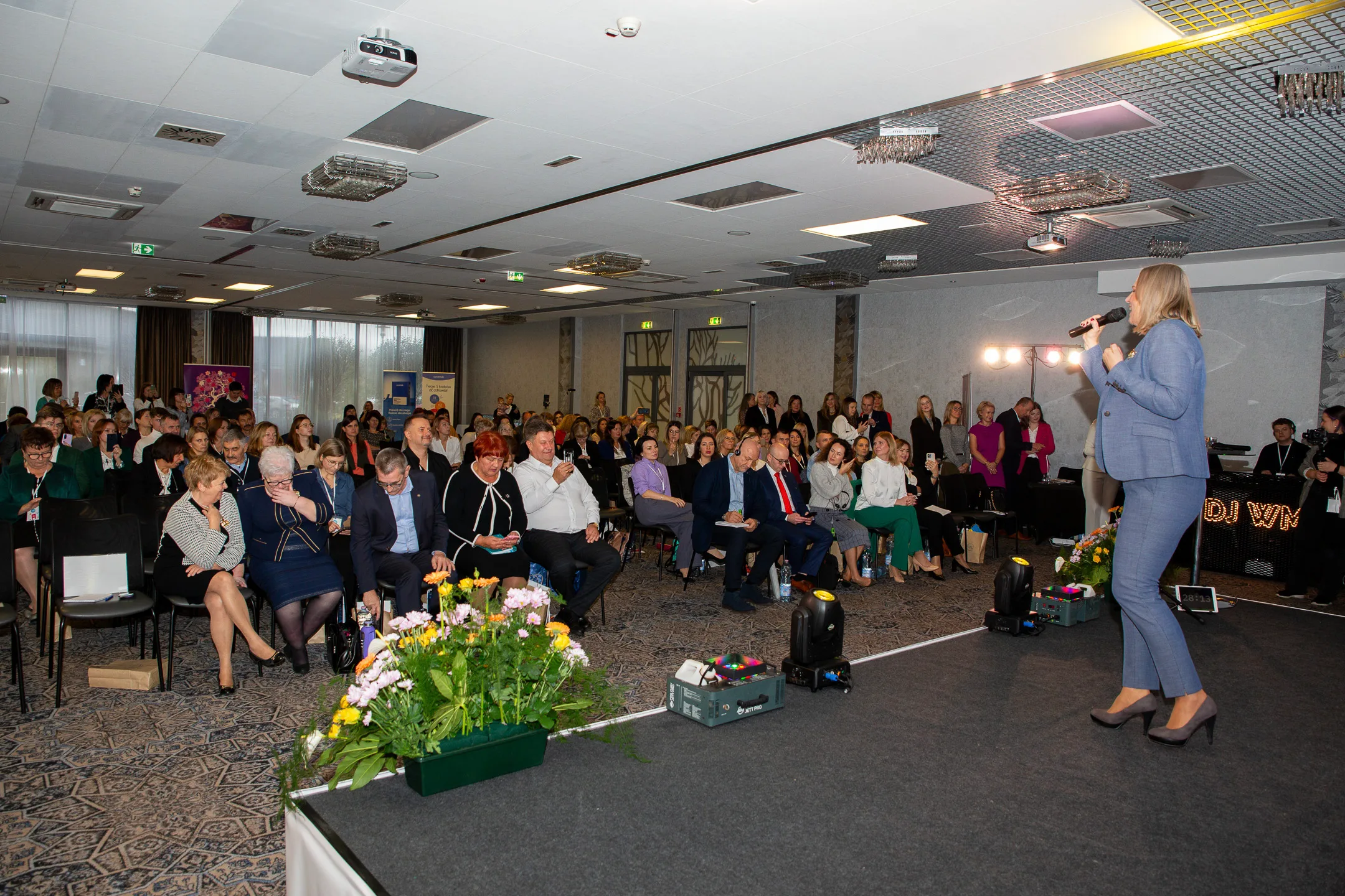 Pełna sala konferencyjna słucha Gosi, która w błękitnym garniturze mówi ze sceny